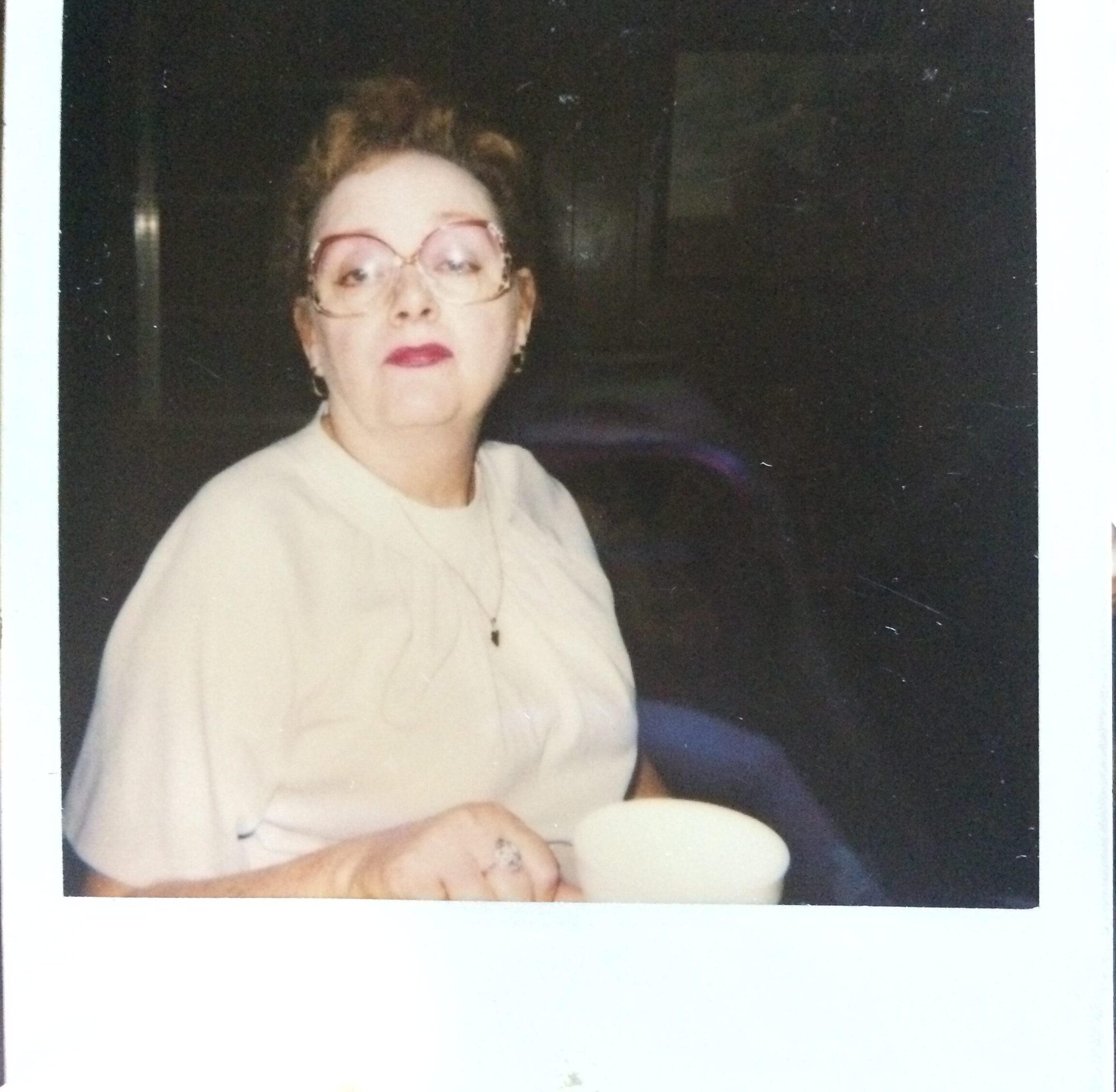 A picture of a Polaroid photo of a sassy looking woman with bright red lipstick and holding a white coffee mug