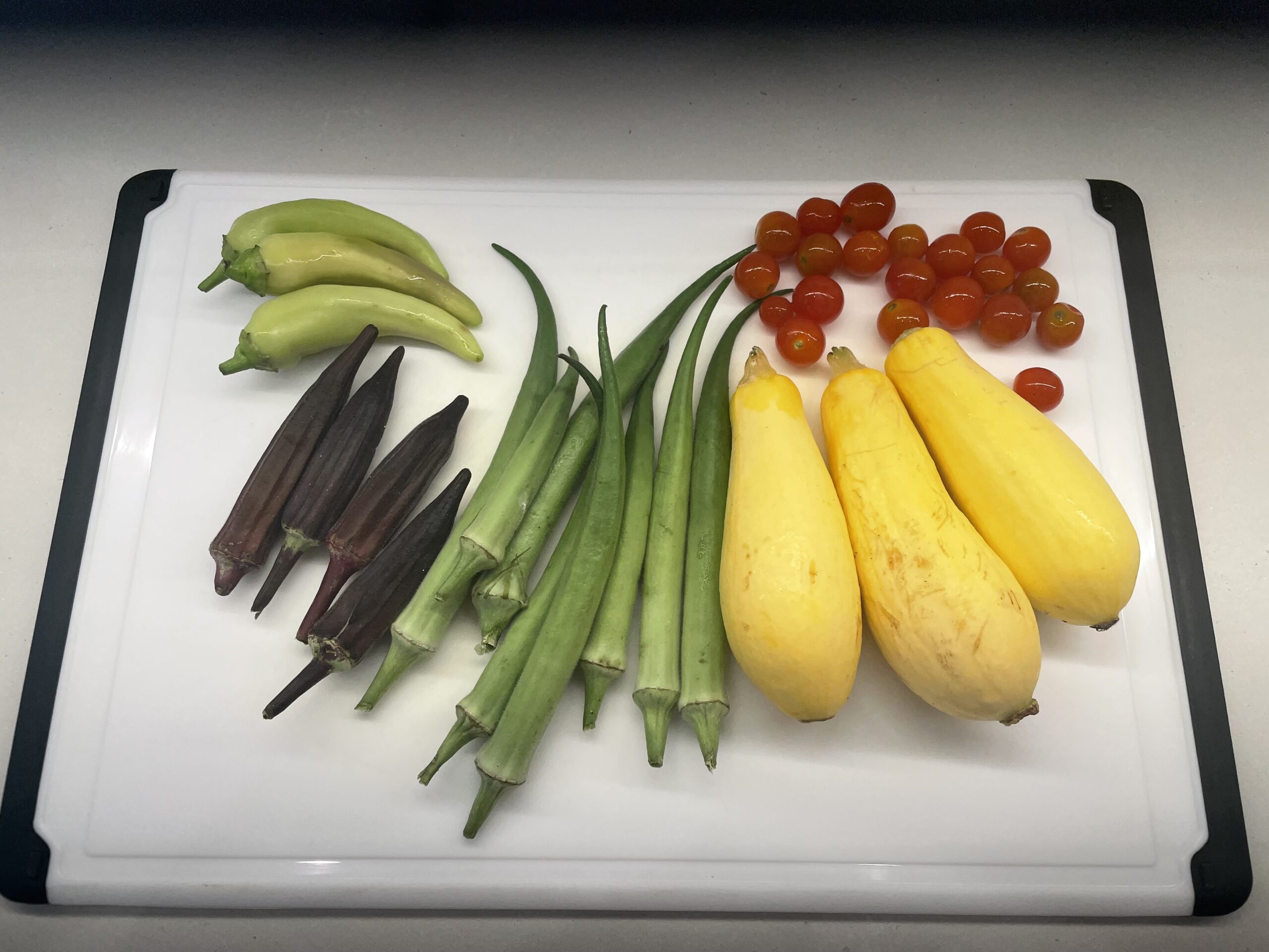 Veggies on a white cutting board - peppers, okra, squash and cherry tomatoes