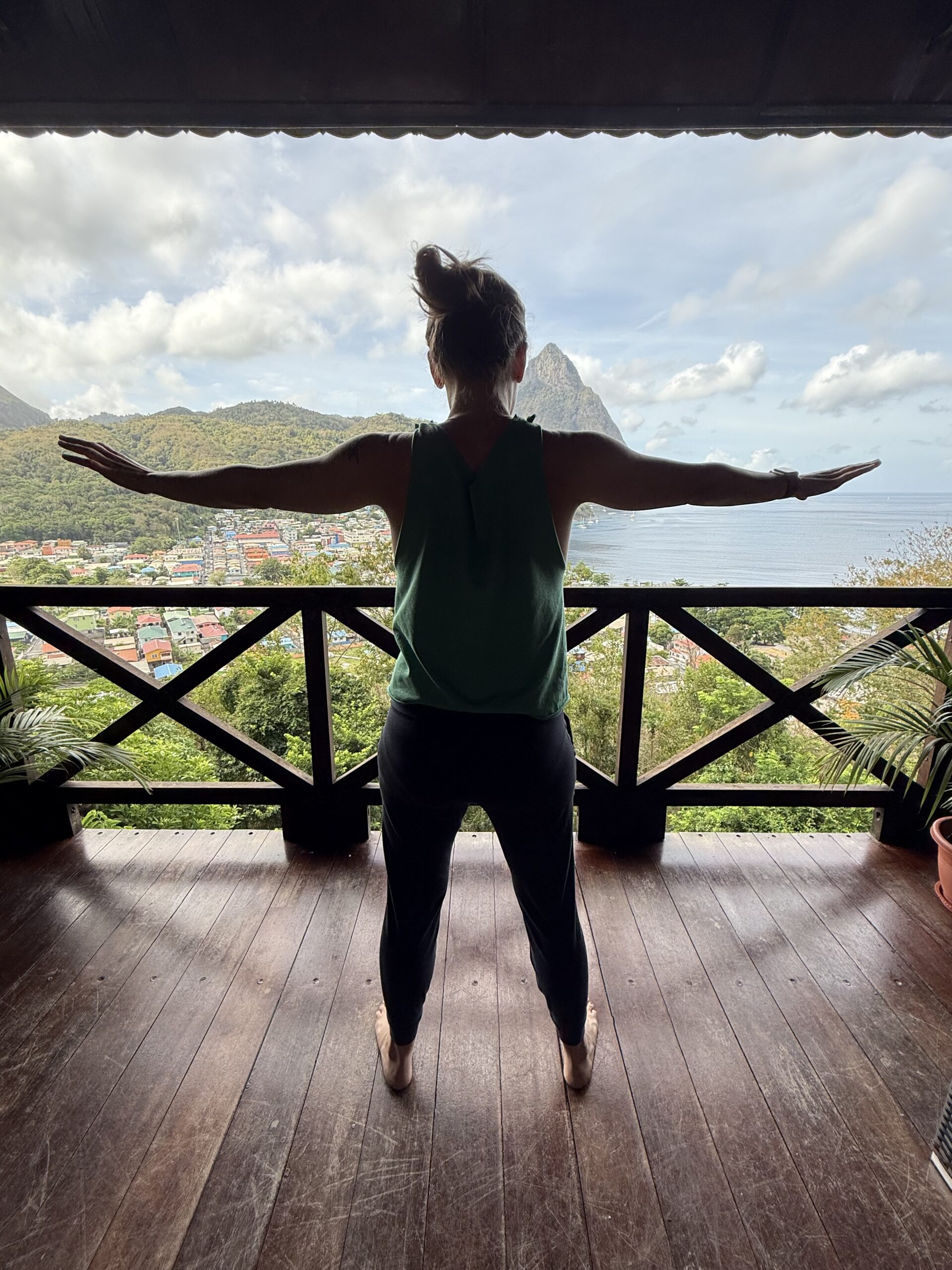 A silhouette of Amber practicing qigong on a balcony overlooking the ocean and the Piton mountains of Saint Lucia