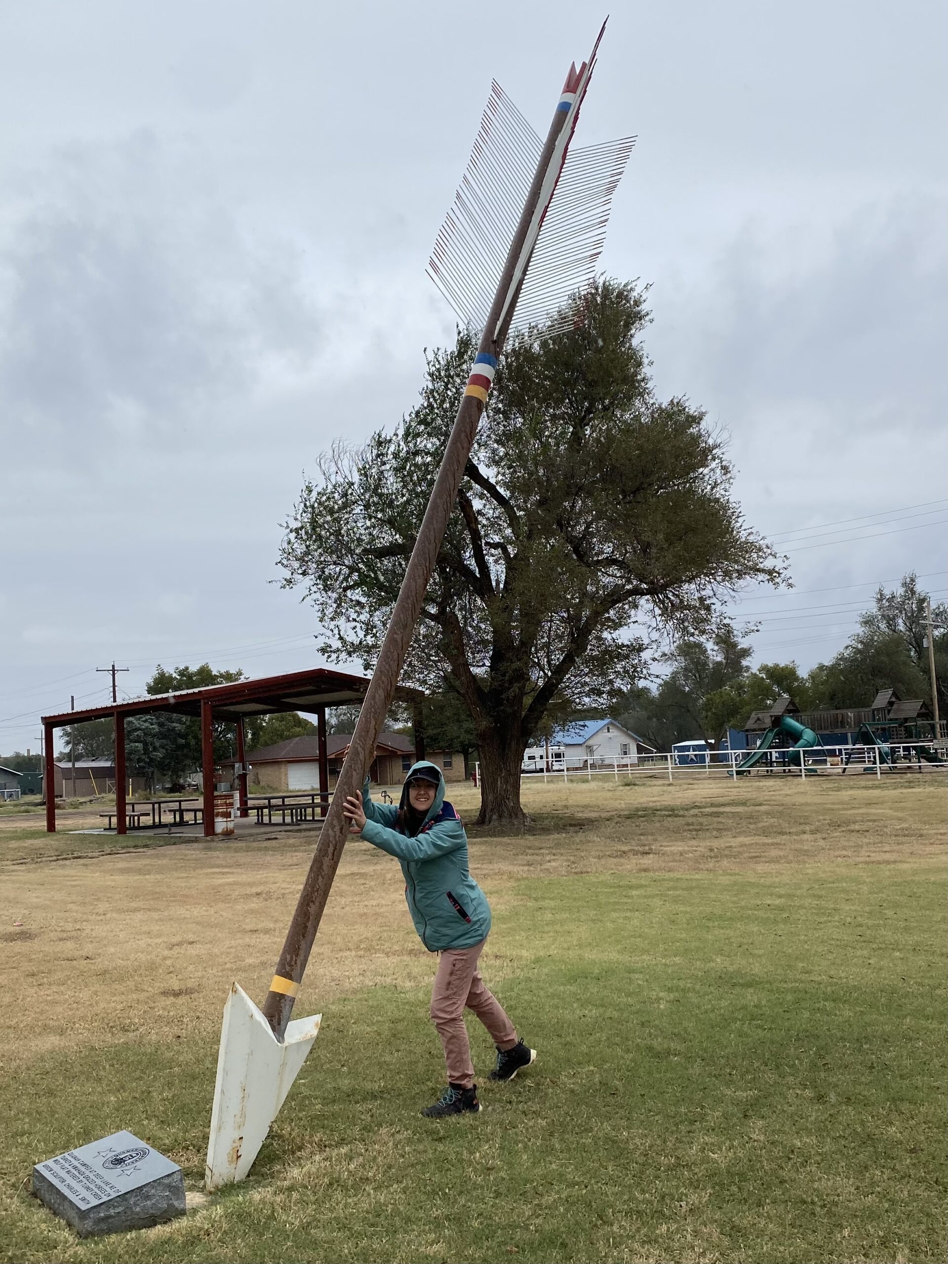 a giant arrow art installation pointing into the grass; Amber pretends to hold it