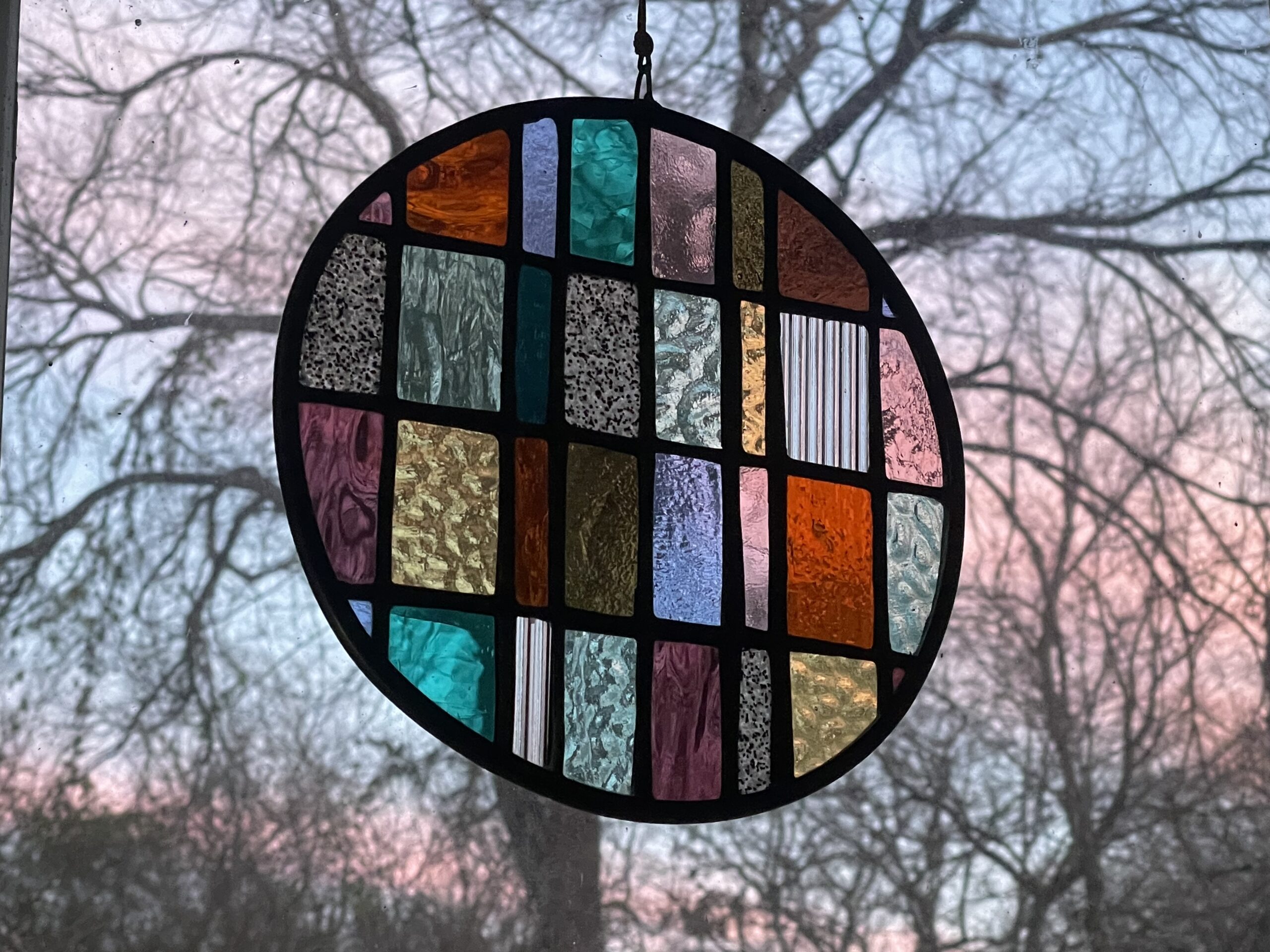 a circular shaped stained glass artwork with a sunset and winter tree in the background