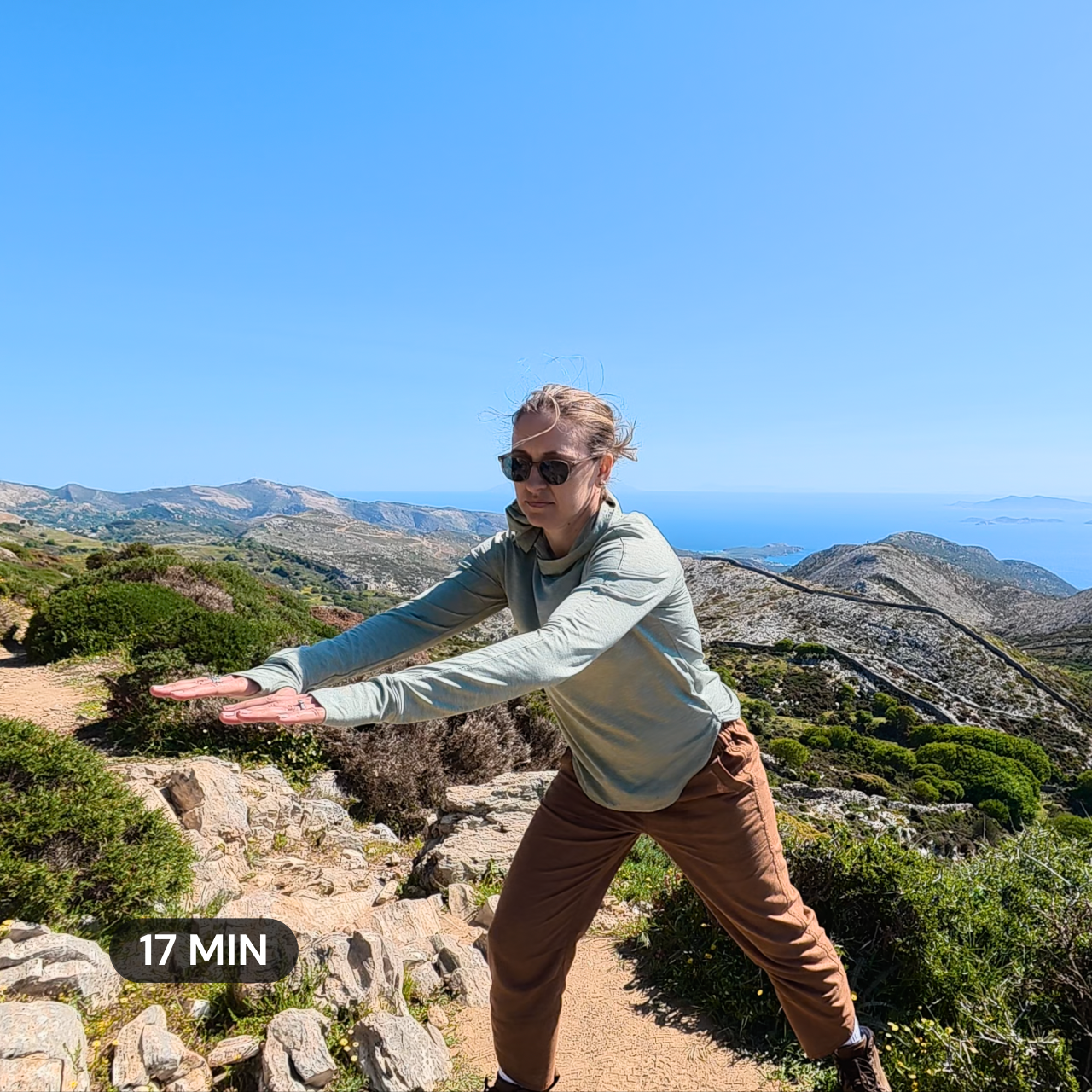 a woman practicing qigong on a mountainside with the Aegean Sea in the background