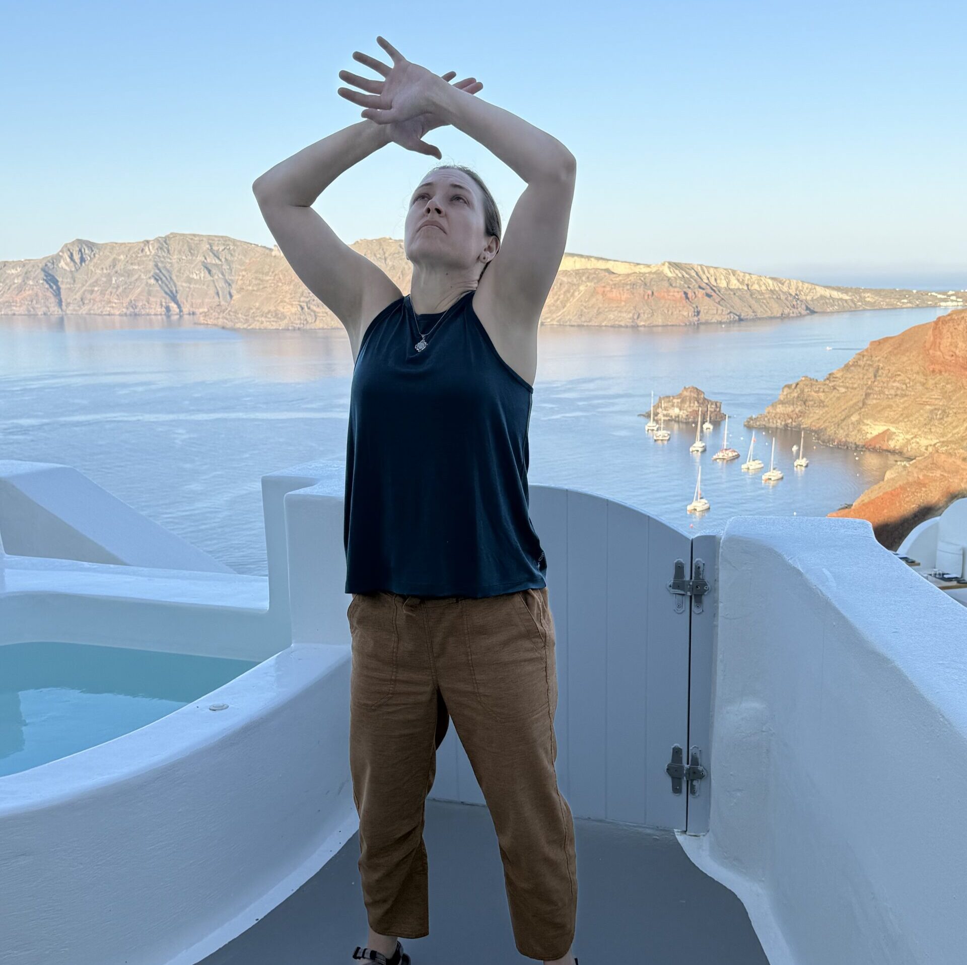 Amber standing with arms overhead, next to a hot tub overlooking the sea in Oia, Santorini, Greece